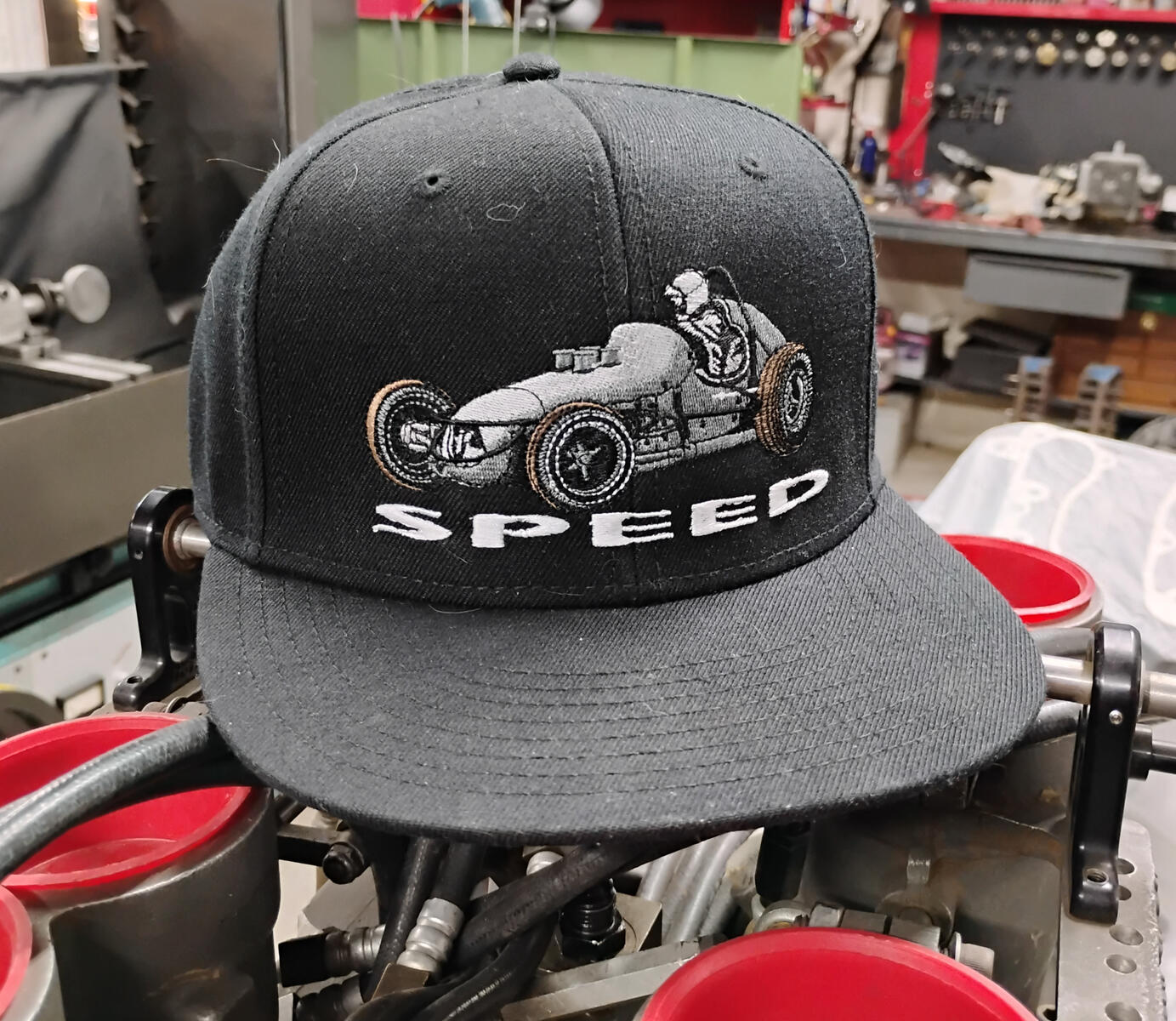 The Speed Sprinter Black pays tribute to an era when sprint cars were raw, lightweight, and unforgiving. Before roll cages. When driving meant commitment. The front features a vintage sprint car with the Speed Shield logo on the side.